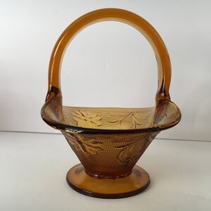 May include: Amber glass basket with a handle and a floral design. The basket has a footed base.