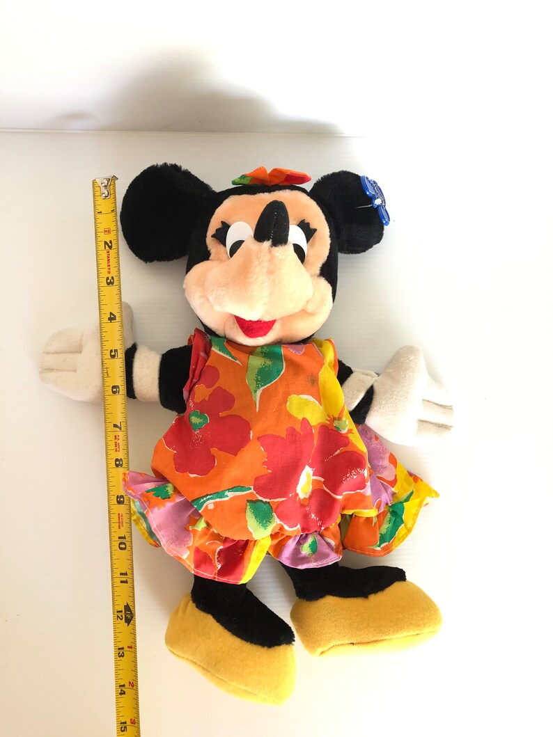 以下が含まれることがあります： 黄色のリボンをつけたカラフルな花柄のドレスを着た、ミニーマウスのぬいぐるみ。人形の高さは約38cmです。