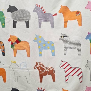 May include: White fabric featuring a repeating pattern of Dala horses in various colours. The horses are decorated with patterns and details, including stars and stripes. The fabric also has some text in the background.