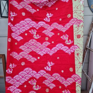 May include: Red fabric with a repeating pattern of white stylized waves and pink fish. The fabric also has small red circles and gold Chinese characters.