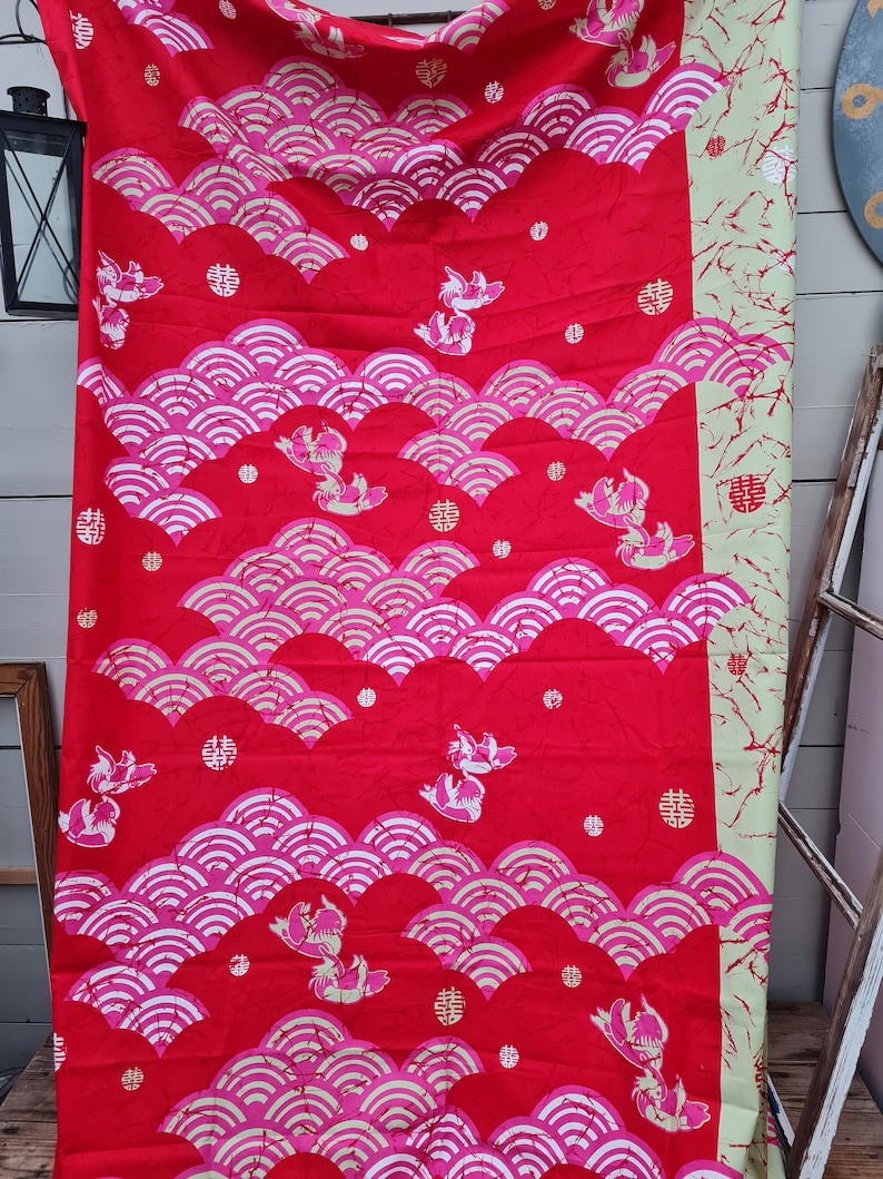 May include: Red fabric with a repeating pattern of white stylized waves and pink fish. The fabric also has small red circles and gold Chinese characters.