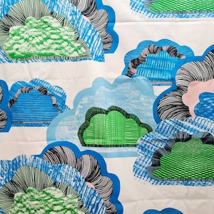 May include: A white fabric with a repeating pattern of blue, green, and black clouds. The clouds are drawn with a scribbled, hand-drawn style.
