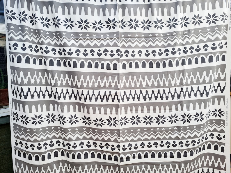 May include: Gray and white fabric with a repeating geometric pattern. The pattern includes snowflakes, arches, and zigzags.