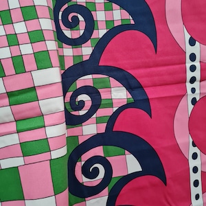Puede incluir: Una tela a cuadros rosa y verde con un diseño azul marino de espirales y curvas. El diseño está sobre un fondo rosa con un borde blanco.