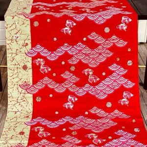 May include: Red fabric with a repeating pattern of pink and white waves and a stylized fish design. The fabric has a gold and white border.