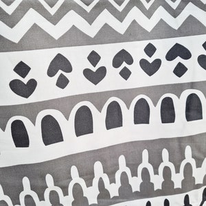 May include: A gray and white fabric with a repeating geometric pattern. The pattern includes hearts, diamonds, arches, and zigzags.