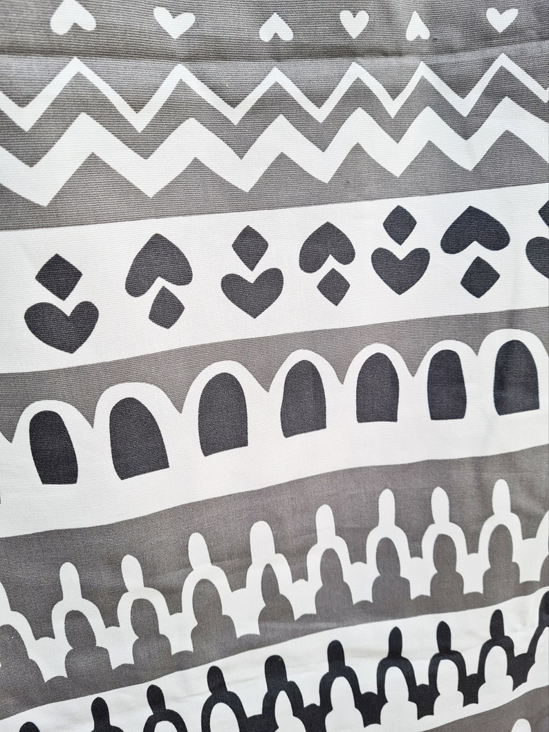 May include: A gray and white fabric with a repeating geometric pattern. The pattern includes hearts, diamonds, arches, and zigzags.
