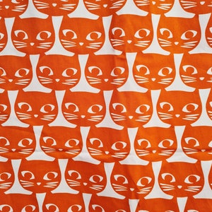May include: Orange fabric with a repeating pattern of white stylized cats. The cats have large eyes and a simple design.