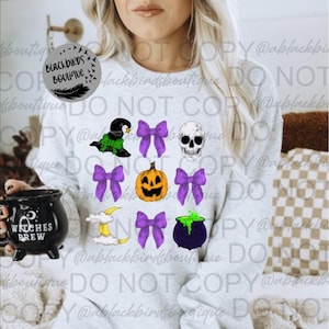 Pode incluir: Uma camisa de frio branca com tema de Halloween que apresenta um chapéu de bruxa, uma caveira, uma abóbora, um caldeirão, uma lua crescente e laços roxos.
