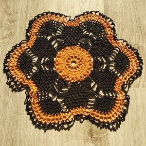 May include: A black and orange crocheted doily with a floral design.