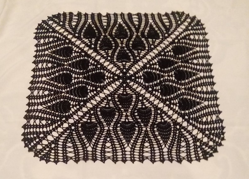 May include: Black crocheted doily with a delicate, intricate design. The doily has a square shape with a central motif of four overlapping circles.