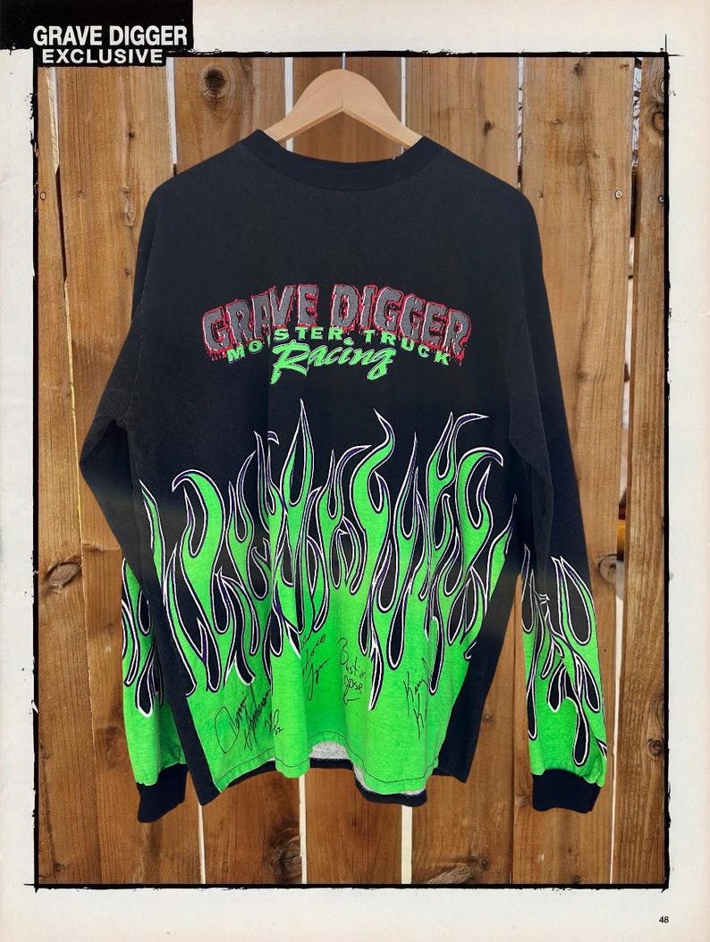 May include: Black long-sleeve shirt featuring a green flame design and the text "Grave Digger Monster Truck Racing." The shirt has signatures and the text "Grave Digger Exclusive" at the top.