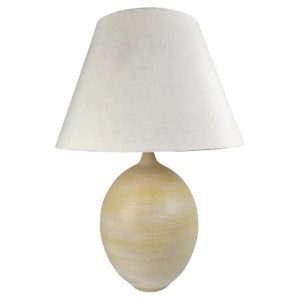 May include: A ceramic table lamp with a white drum shade. The lamp base is a round, off-white ceramic with a textured finish.