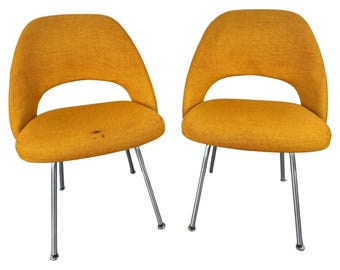 May include: Two mustard yellow chairs with a mid-century modern design. The chairs have a curved back and a wide seat. The chairs are supported by four thin metal legs.