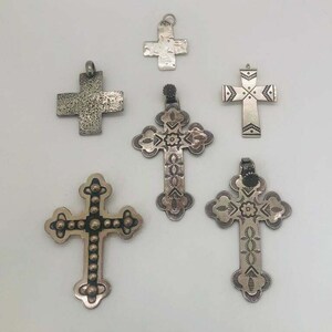 May include: Six silver cross pendants with various designs. Some crosses have a textured finish, while others have intricate patterns.
