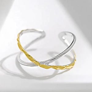 May include: A silver and gold ring with a twisted design. The ring is made of two bands, one silver and one gold, that are twisted together.