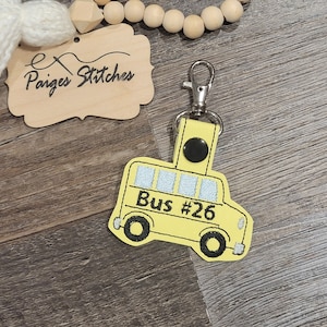 May include: Yellow school bus keychain with the text "Bus #26" on the side. The keychain has a silver metal ring and a black button.
