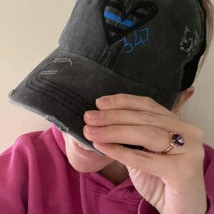 May include: A black distressed baseball cap with a blue and black heart design and the number 347 embroidered on the front. The cap has a mesh back.