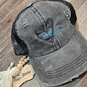 May include: A black distressed trucker hat with a blue and black heart and the number 347 embroidered on the front. The hat has a mesh back.