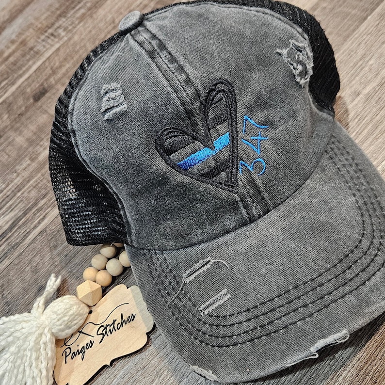 May include: A black distressed trucker hat with a blue and black heart and the number 347 embroidered on the front. The hat has a mesh back.