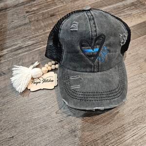 May include: A black and gray distressed trucker hat with a blue line heart and the number 347 embroidered on the front. The hat has a mesh back.