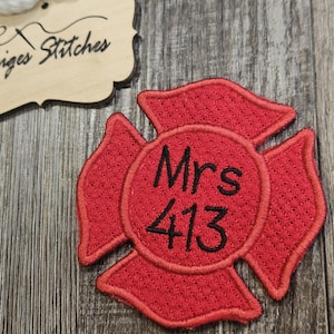 May include: Red embroidered firefighter's badge with the text "Mrs. 413" in black thread.
