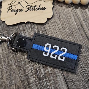 May include: Black leather keychain with a blue thin blue line and the number 922 in white.