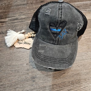 May include: Black distressed trucker hat with a blue line heart and the number 347 embroidered on it.