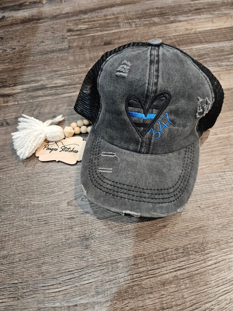 May include: Black distressed trucker hat with a blue line heart and the number 347 embroidered on it.