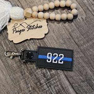 May include: Black leather keychain with a blue thin blue line and the number 922 in white.