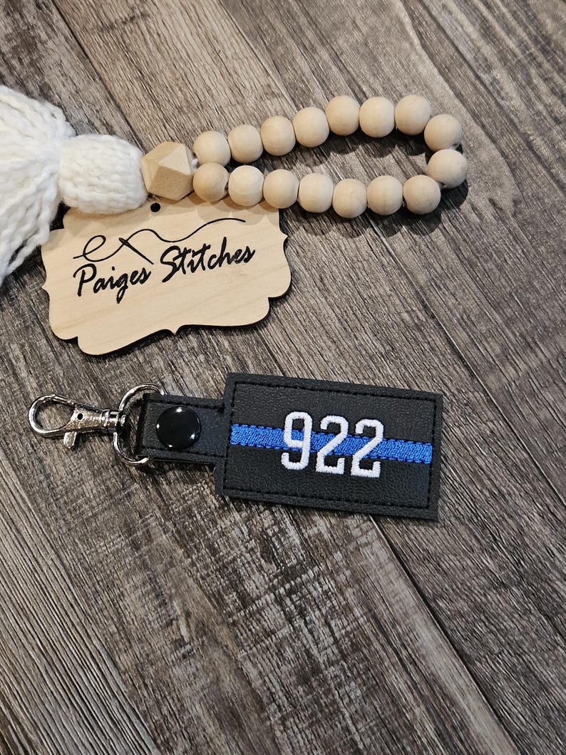 May include: Black leather keychain with a blue thin blue line and the number 922 in white.