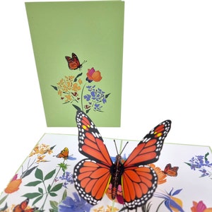 Peut inclure: Une carte pop-up 3D repr&eacute;sentant un grand papillon orange et noir avec ses ailes d&eacute;ploy&eacute;es. Le papillon est entour&eacute; d'un motif floral de feuilles vertes et de fleurs color&eacute;es.