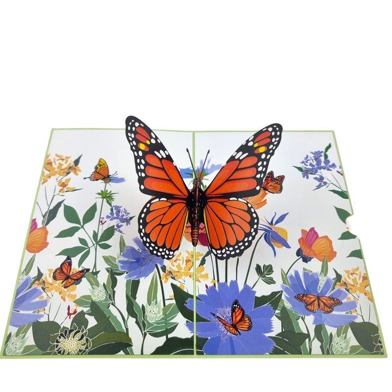 Peut inclure: Une carte pop-up 3D repr&eacute;sentant un papillon monarque aux ailes orange et noires, entour&eacute; de fleurs color&eacute;es et de verdure.