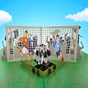 Könnte beinhalten: Eine Pop-up-Karte mit einem Fußballmotiv, die einen 3D-Fußball und zwei Spieler in Aktion zeigt. Die Spieler tragen orangefarbene und blaue Trikots, mit einem Tor und einer Menschenmenge im Hintergrund. Die Karte befindet sich auf einem grünen Feld mit blauem Himmel.