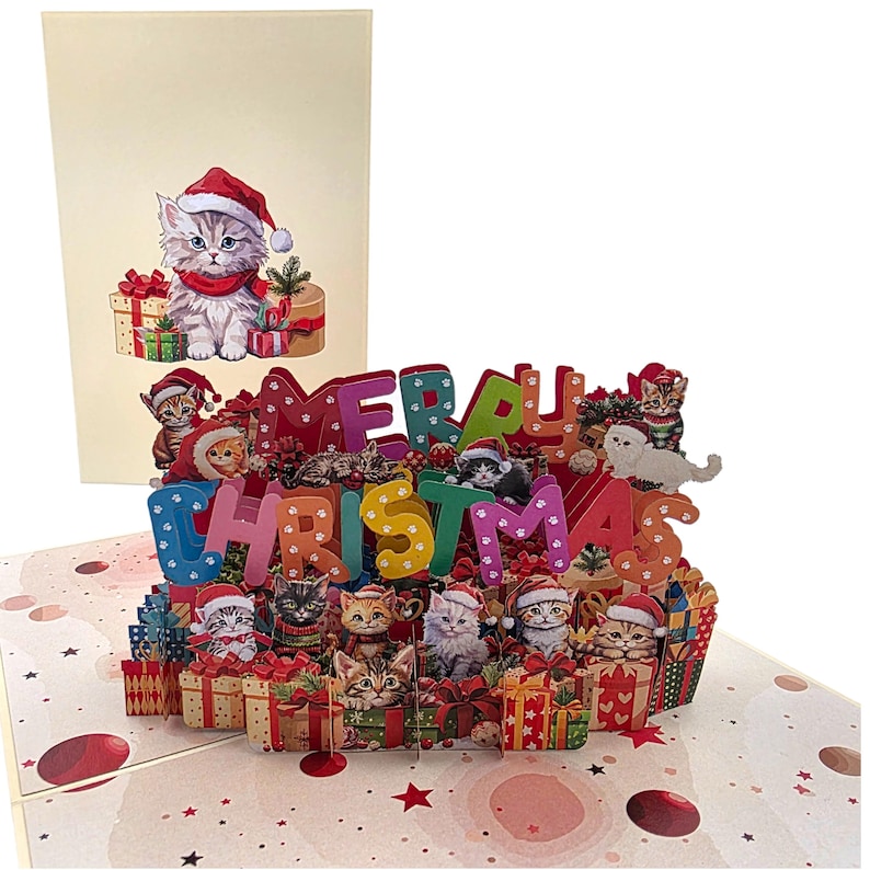 Peut inclure: Carte de No&euml;l pop-up avec un design festif. Elle pr&eacute;sente des chatons portant des chapeaux de P&egrave;re No&euml;l et entour&eacute;s de cadeaux. La carte &eacute;pelle "MERRY CHRISTMAS" en lettres color&eacute;es. Un chaton assorti est sur le devant.