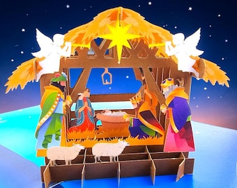 Può includere: Un biglietto pop-up tridimensionale che raffigura una scena della natività con una mangiatoia centrale, figure in vesti colorate, due pecore bianche e due angeli bianchi sul tetto sotto una stella gialla brillante.