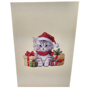 Peut inclure: Carte de v&oelig;ux sur le th&egrave;me de No&euml;l avec un chaton de dessin anim&eacute; portant un bonnet de P&egrave;re No&euml;l et une &eacute;charpe rouge. Le chaton est entour&eacute; de cadeaux emball&eacute;s avec des n&oelig;uds rouges et une petite branche de conif&egrave;re. La carte a un fond cr&egrave;me.