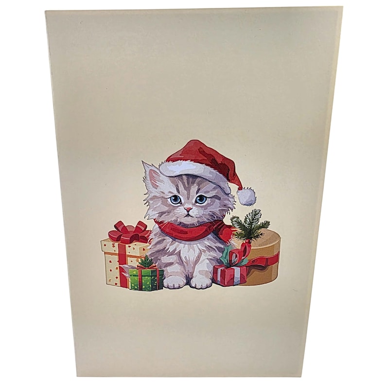 Peut inclure: Carte de v&oelig;ux sur le th&egrave;me de No&euml;l avec un chaton de dessin anim&eacute; portant un bonnet de P&egrave;re No&euml;l et une &eacute;charpe rouge. Le chaton est entour&eacute; de cadeaux emball&eacute;s avec des n&oelig;uds rouges et une petite branche de conif&egrave;re. La carte a un fond cr&egrave;me.