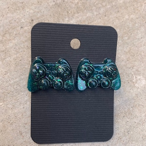 May include: A pair of green glitter resin earrings shaped like video game controllers.