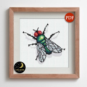 May include: Cross-stitch pattern of a fly with red eyes, green body, and gray wings, framed in a light brown wooden frame. The image includes a PDF icon and a Luna River Crafts logo.