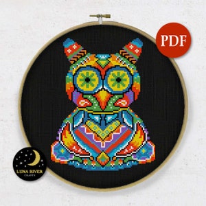 May include: A colorful cross-stitch pattern of an owl, featuring vibrant hues of blue, green, orange, and yellow. The owl is set against a black background within a wooden embroidery hoop. A red PDF button is in the upper right corner.