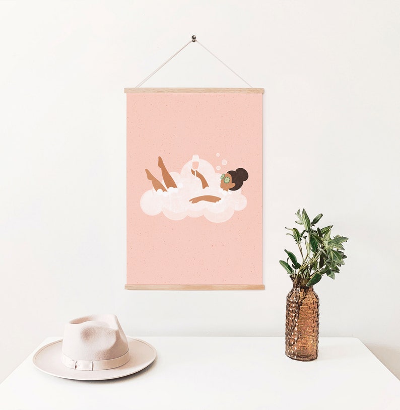 May include: A pink framed print with a cartoon illustration of a person relaxing in a bubble bath with a glass of champagne. The person is wearing a pair of green eye masks.