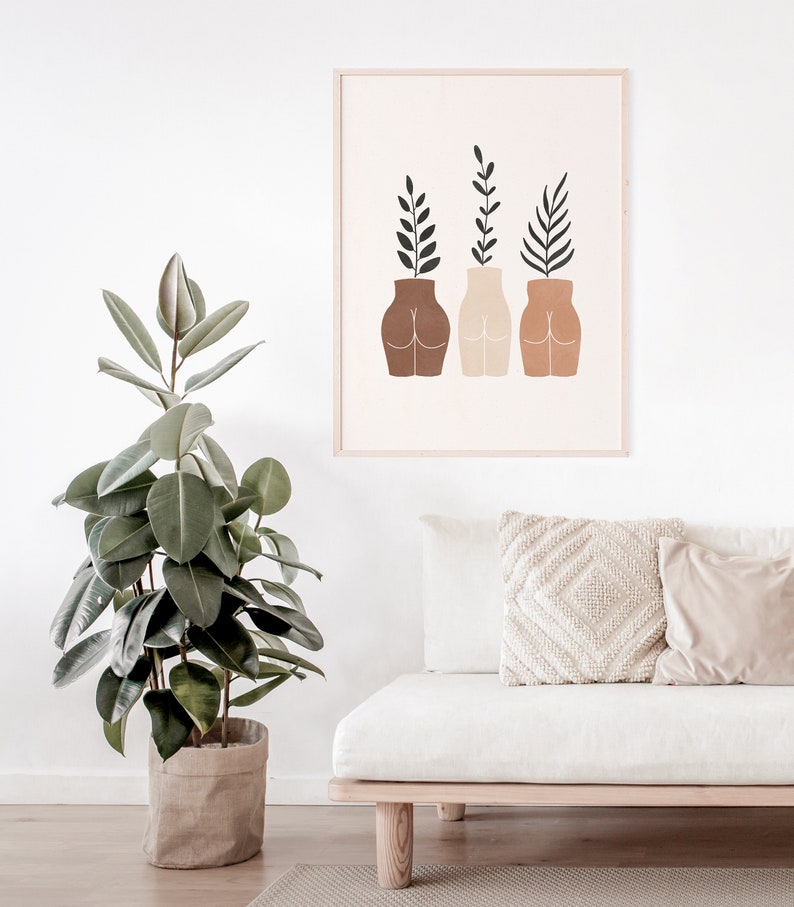 May include: A framed print with a minimalist design featuring three stylized figures with plants growing out of their heads. The figures are in shades of brown, beige, and peach.
