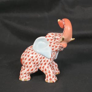 May include: A ceramic elephant figurine with a red and white patterned body, light blue ears, and a raised pink trunk. The figurine has gold accents on its feet and trunk. The elephant is a decorative item.