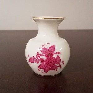 May include: A small white porcelain vase with a pink floral design. The vase has a round body and a narrow neck.
