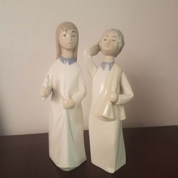 pair of Rex Valencia hand-painted porcelain figurines of a girl holding a candlestick and a boy with a towel or blanket over his shoulder