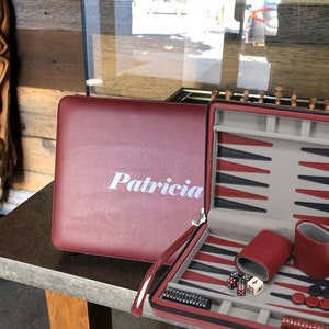 May include: A red leather carrying case for a backgammon set. The case is open and shows the backgammon board, dice, and checkers. The case is personalized with the name "Patricia".