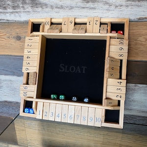 May include: A wooden game board with a black felt playing surface and numbered wooden tiles. The game board is labeled "SLOAT" and has dice in various colors.