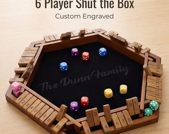 May include: A hexagonal wooden Shut the Box game board for 6 players with a black felt interior, numbered wooden tiles, and colorful dice. The center is engraved with the text The Dunn Family, and the top displays 6 Player Shut the Box Custom Engraved.