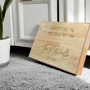 May include: A wooden box with the text "The Mitchells" and "EST. 2024" engraved on the top. The coordinates "34.01735° N 118.28876° W" are also engraved on the box.